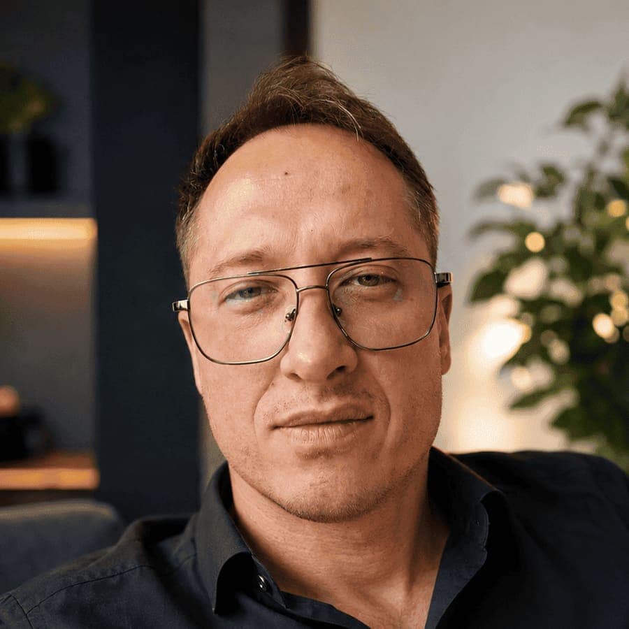 Daniel Kuk w okularach i ciemnej koszuli, w ciepło oświetlonym wnętrzu.